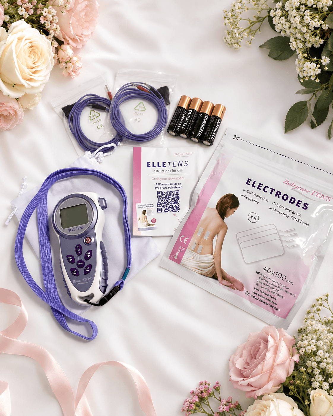 The Coastal Birth Co. labour TENS hire kit laid out — Elle TENS machine with lanyard, two lead wires, self-adhesive maternity electrode pads, AA batteries and instruction manual, styled with soft roses and linen.